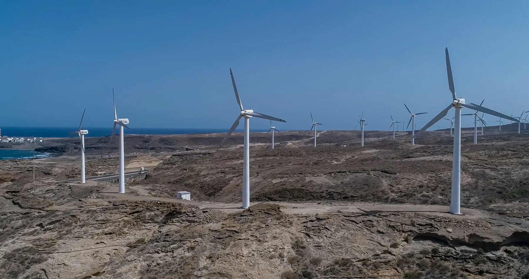 Wind turbines along a bare stretch of coast under a grey sky