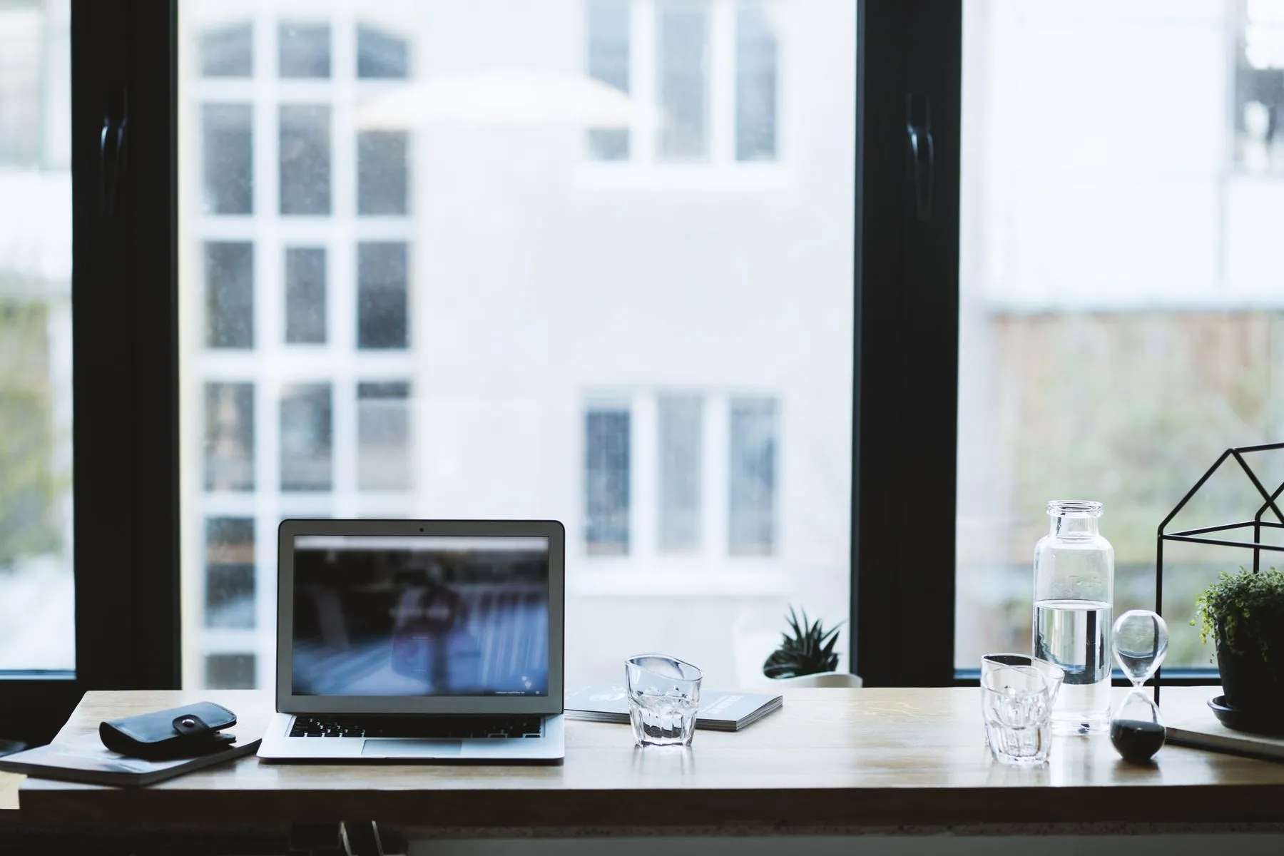 A tidy desk with an open laptop by a tall window